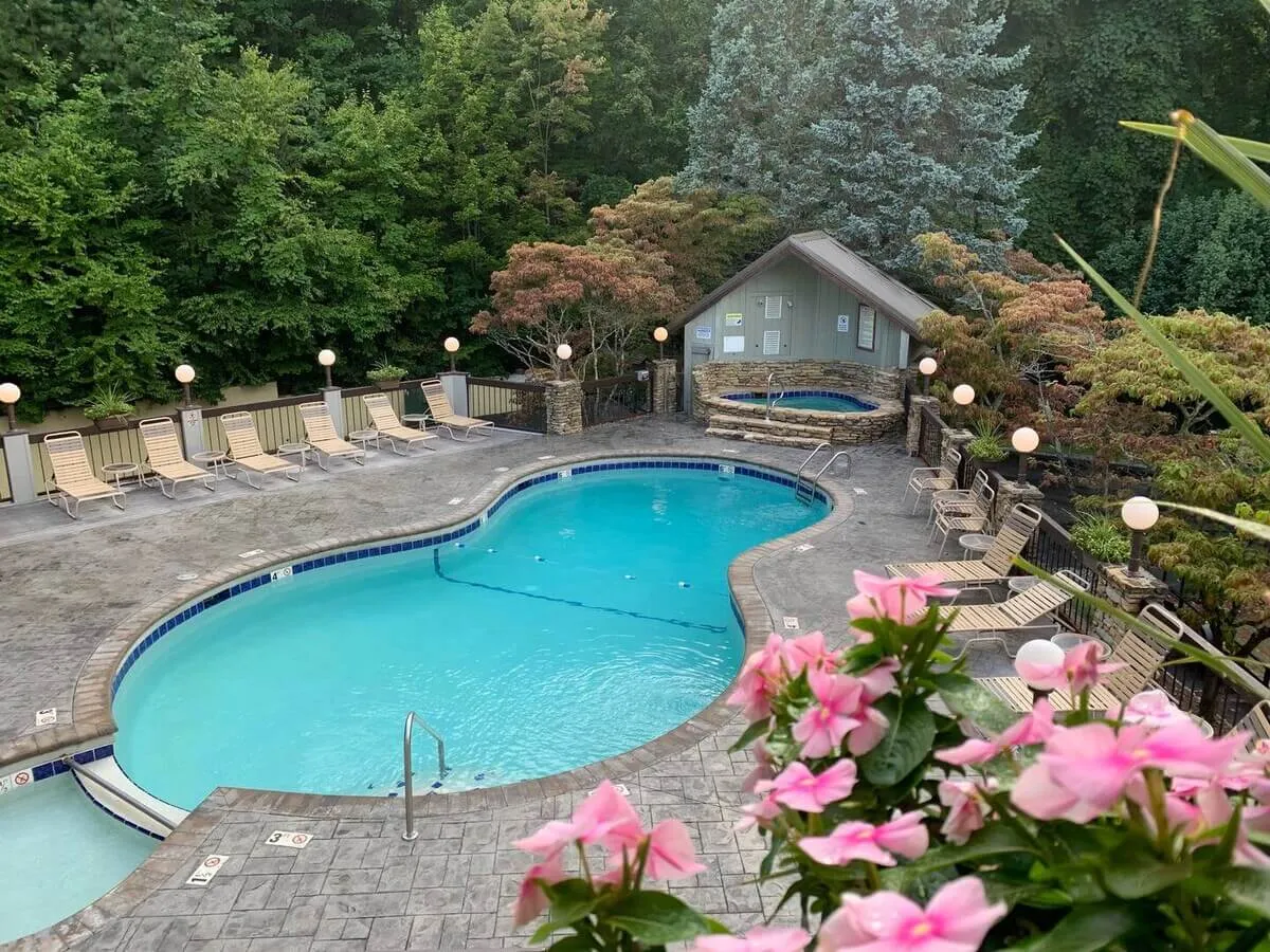 A beautiful outdoor pool area featuring a sparkling swimming pool, adjacent jacuzzi, and comfortable lounge chairs arranged for both sunbathing and socializing. The scene includes vibrant floral arrangements and captures the warm glow of sunset, with a tranquil and inviting atmosphere ideal for both relaxation and gatherings.