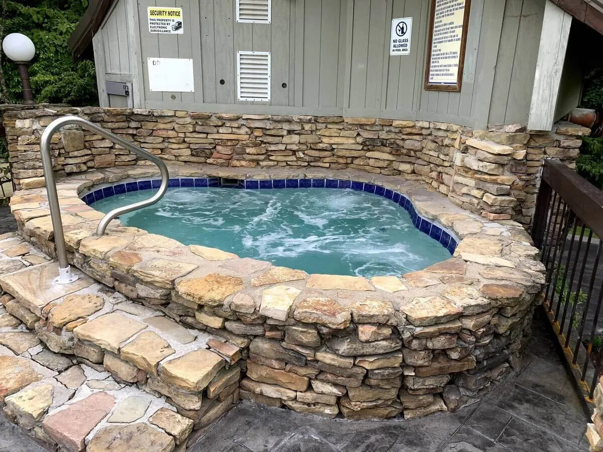 A serene hot tub area bordered by a rustic stone wall and accessed via gentle steps. The hot tub is set against a tranquil backdrop, inviting relaxation and intimate conversations, especially suited for après-ski or stargazing.