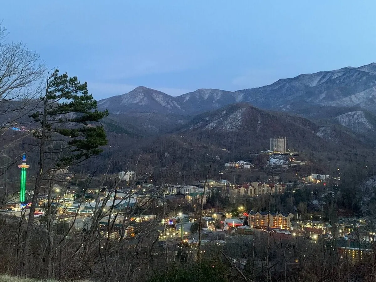 A sweeping view of the Smoky Mountains at sunset, with city lights beginning to twinkle and an amusement park in the distance. The vantage point suggests a private balcony or overlook, perfect for soaking in romantic sunrises and sunsets with a loved one.