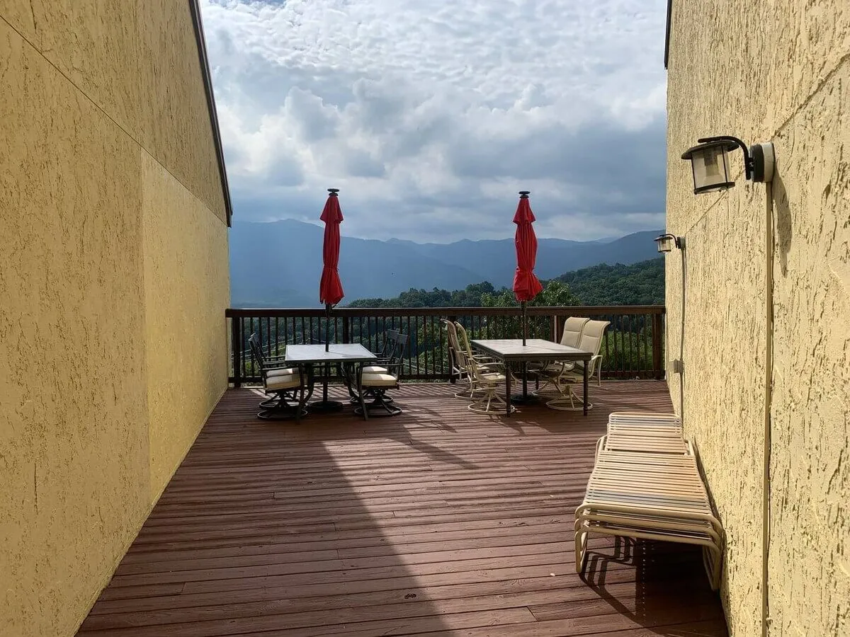 An expansive deck area with tables shaded by umbrellas, offering panoramic mountain views. The deck provides a serene space for outdoor dining, family games, or simply soaking in the sunset over the peaks.