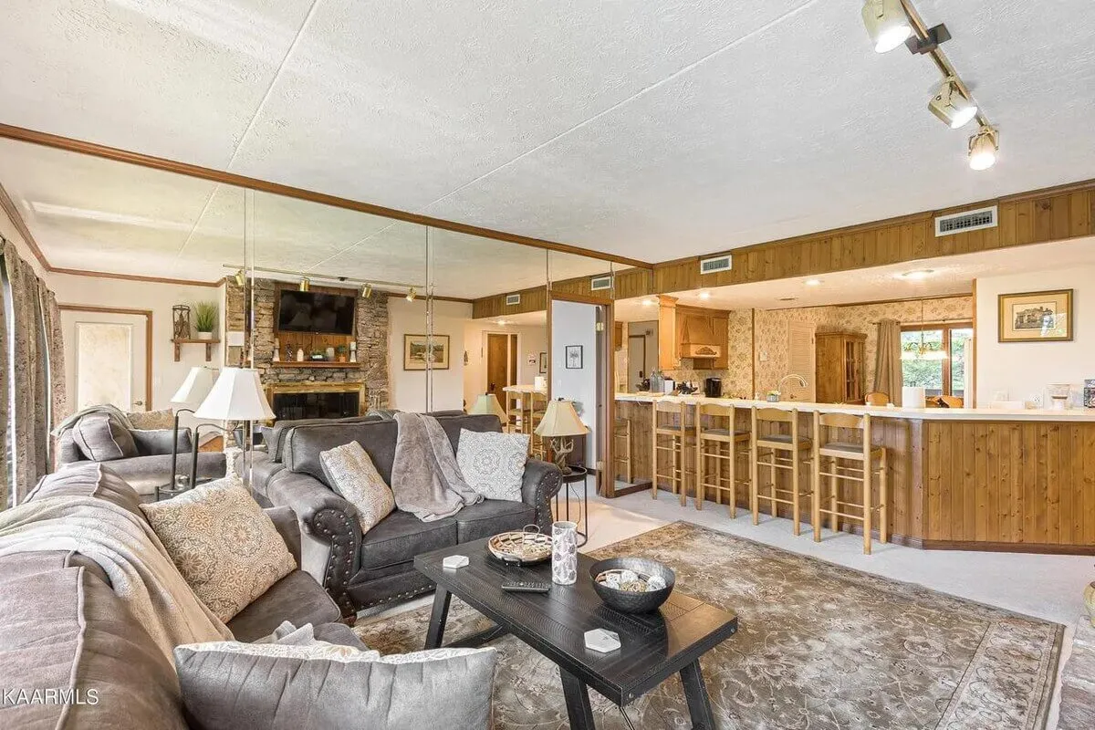 A spacious and inviting living area with a plush sofa facing a fireplace, seamlessly connected to a kitchen bar area. The design encourages social interaction, with comfortable seating for gatherings and warm, ambient lighting creating a welcoming mood.