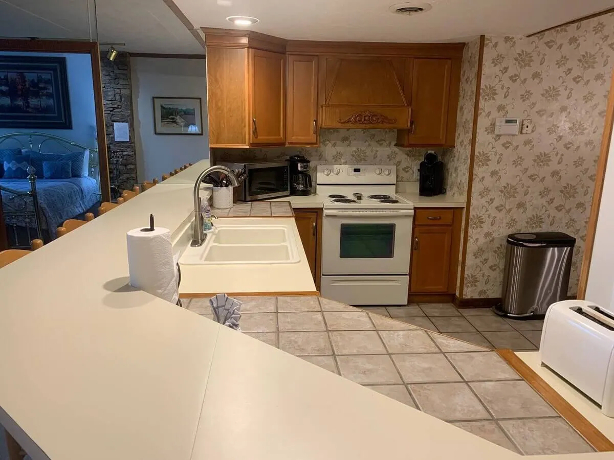 A cozy kitchen scene featuring a spacious countertop, modern appliances, a sink, and three inviting bar stools. Warm lighting and practical layout create a welcoming space for cooking and entertaining, while details like the bar stools hint at casual gatherings and morning routines.
